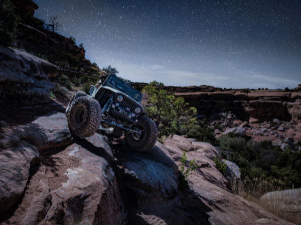 A driver is driving a Grey Jeep Wrangler Across Rocks