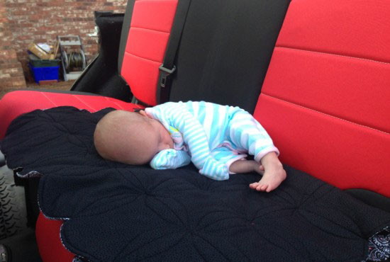 A cute baby is sleeping on jeep wrangler back seat